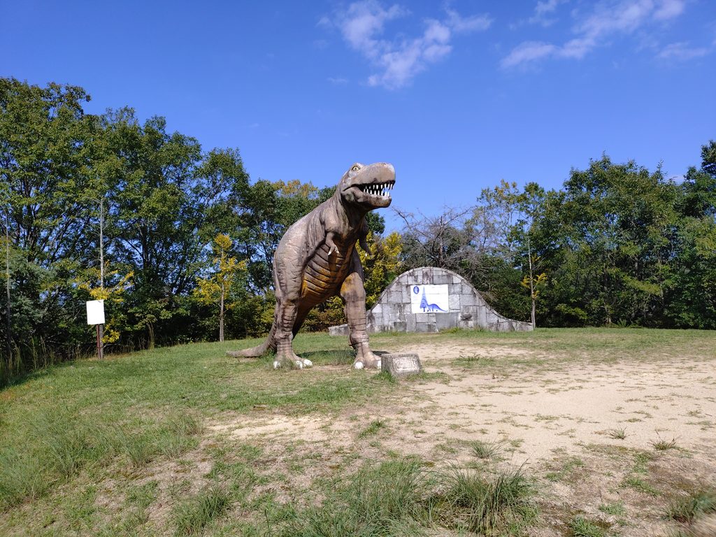 園内のティラノサウルスがいる広場の様子とティラノサウルスを捉えた写真。奥には園内に植えられているメタセコイヤにまつわる情報が記載された石碑がある